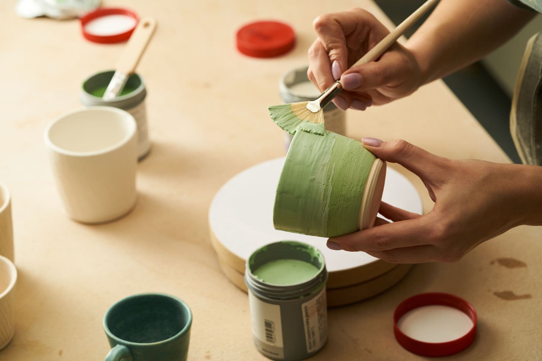 A hand painting a ceramic mug in soft green glaze